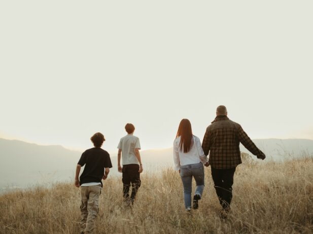 family of four strolling on an open field with a sunny sky